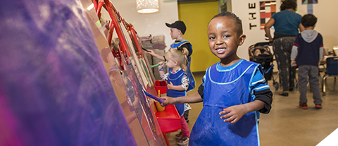 child in smock painting at an easel
